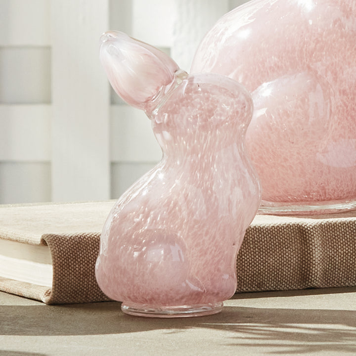 Pink glass bunny-shaped sculpture on a wooden surface with a blurred background