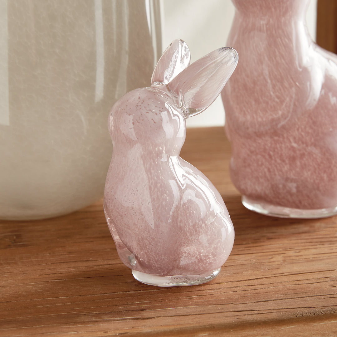 Pink glass bunny figurine on a wooden surface with a blurred background