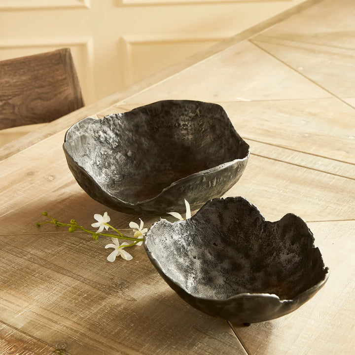 Two black aluminum bowls on a wooden surface with small white flowers.