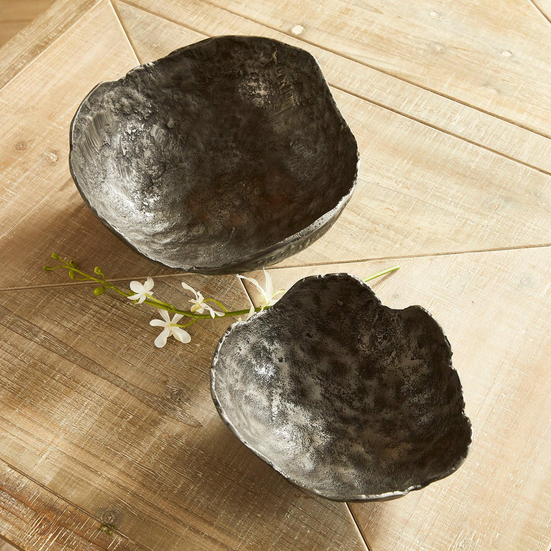 Two dark bowls on a wooden surface with small white flowers.