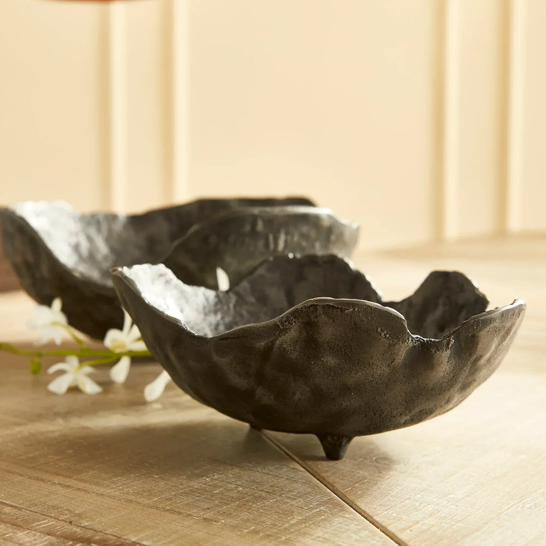 Two dark metal leaf-shaped bowls on a wooden surface with a light background