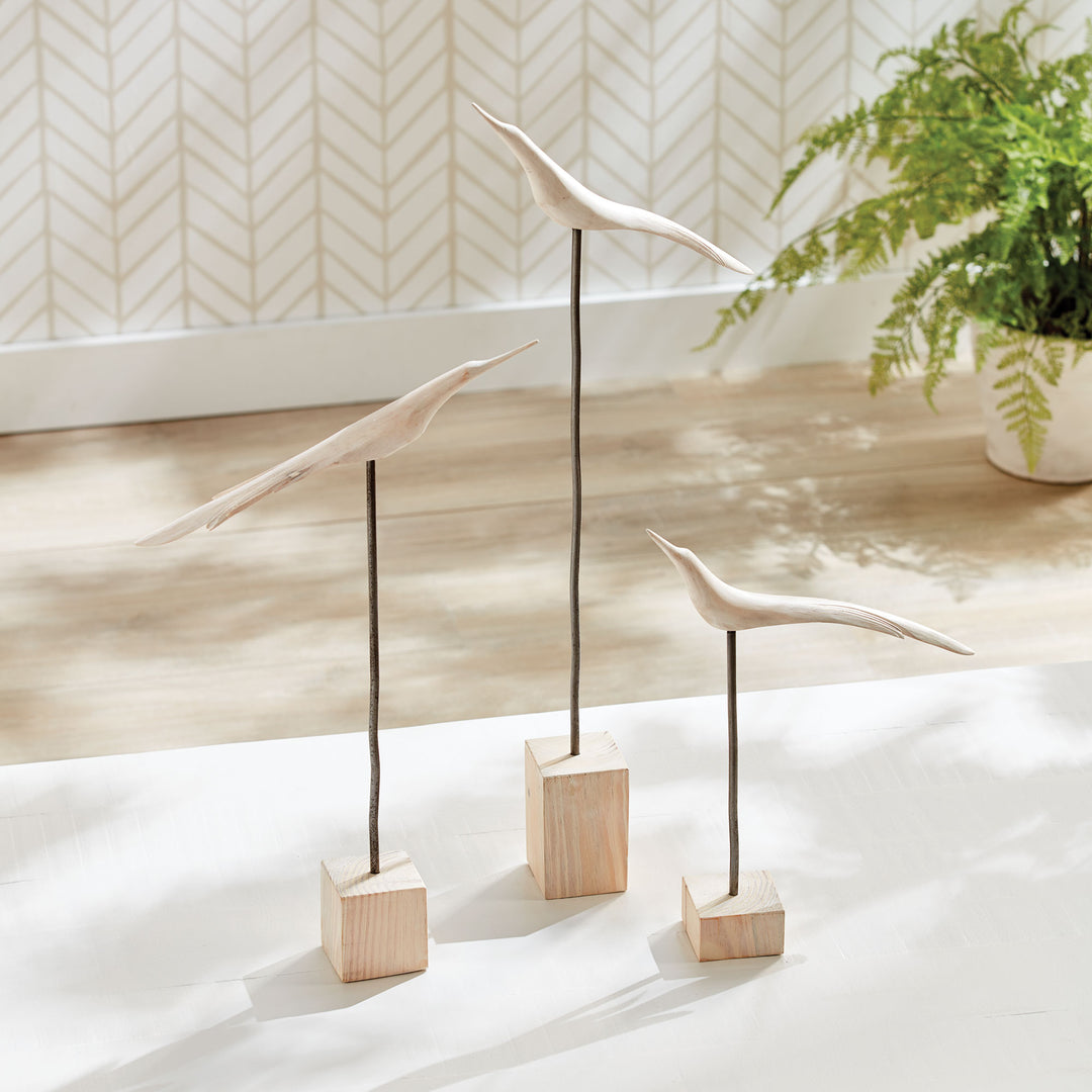 Decorative bird sculptures on wooden blocks with a plant in the background