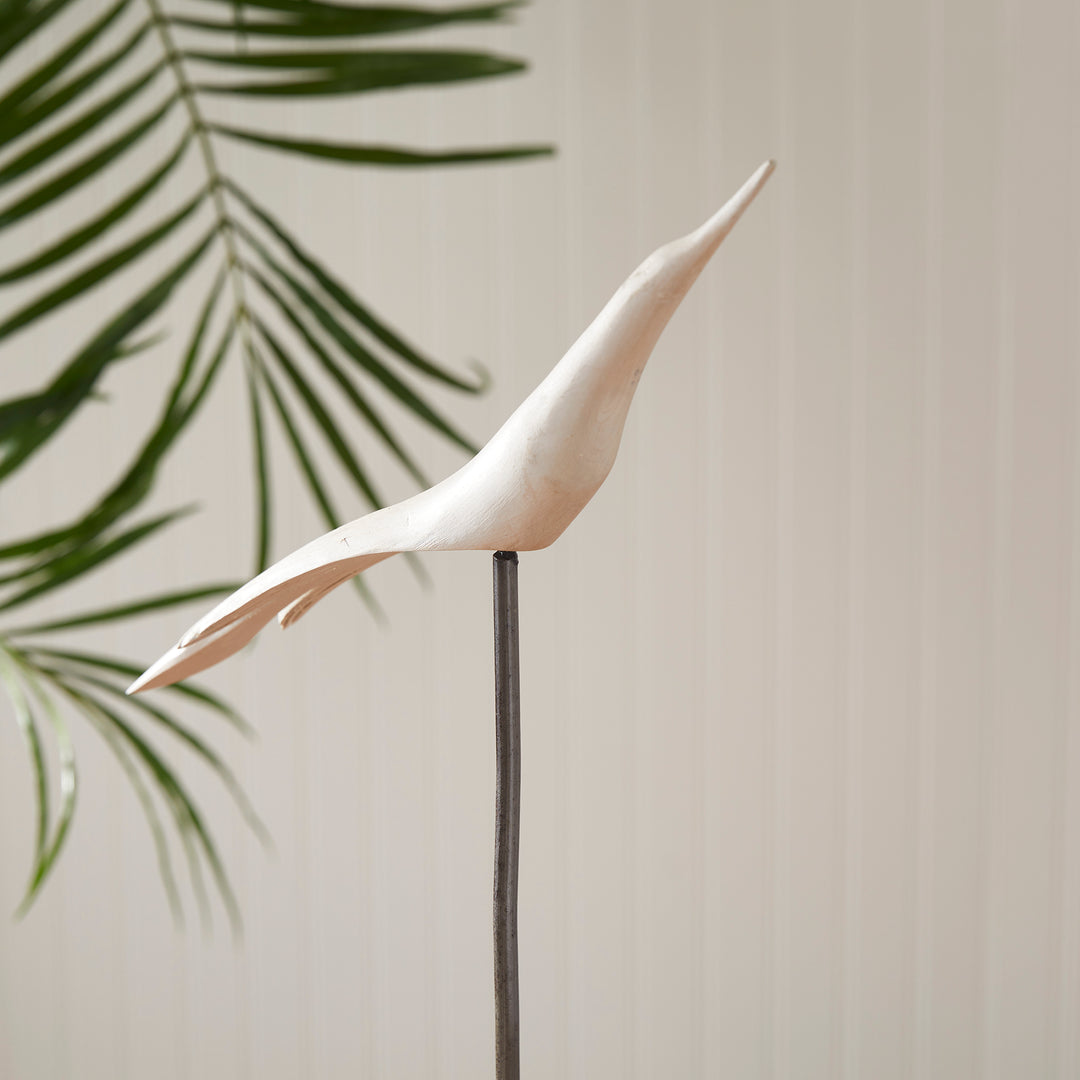 Decorative white bird sculpture on a stand with green leaves in the background