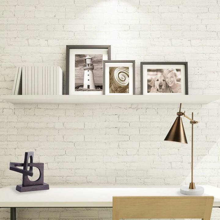Framed pictures on a shelf against a white brick wall with a lamp and decor items.