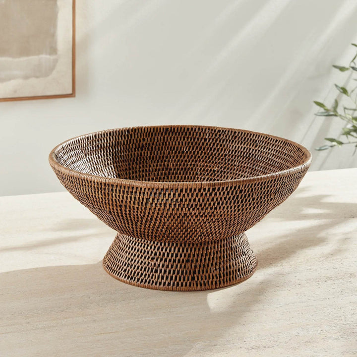 Empty warm brown woven rattan pedestal offering bowl displayed on a pale console beneath simple framed artwork, Transitional