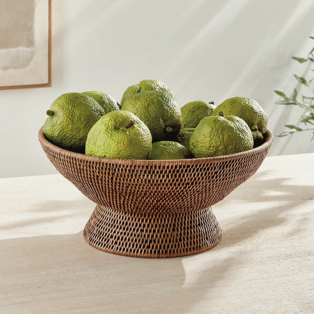 Warm brown woven rattan pedestal offering bowl filled with green fruit on a light console in a neutral room, Transitional