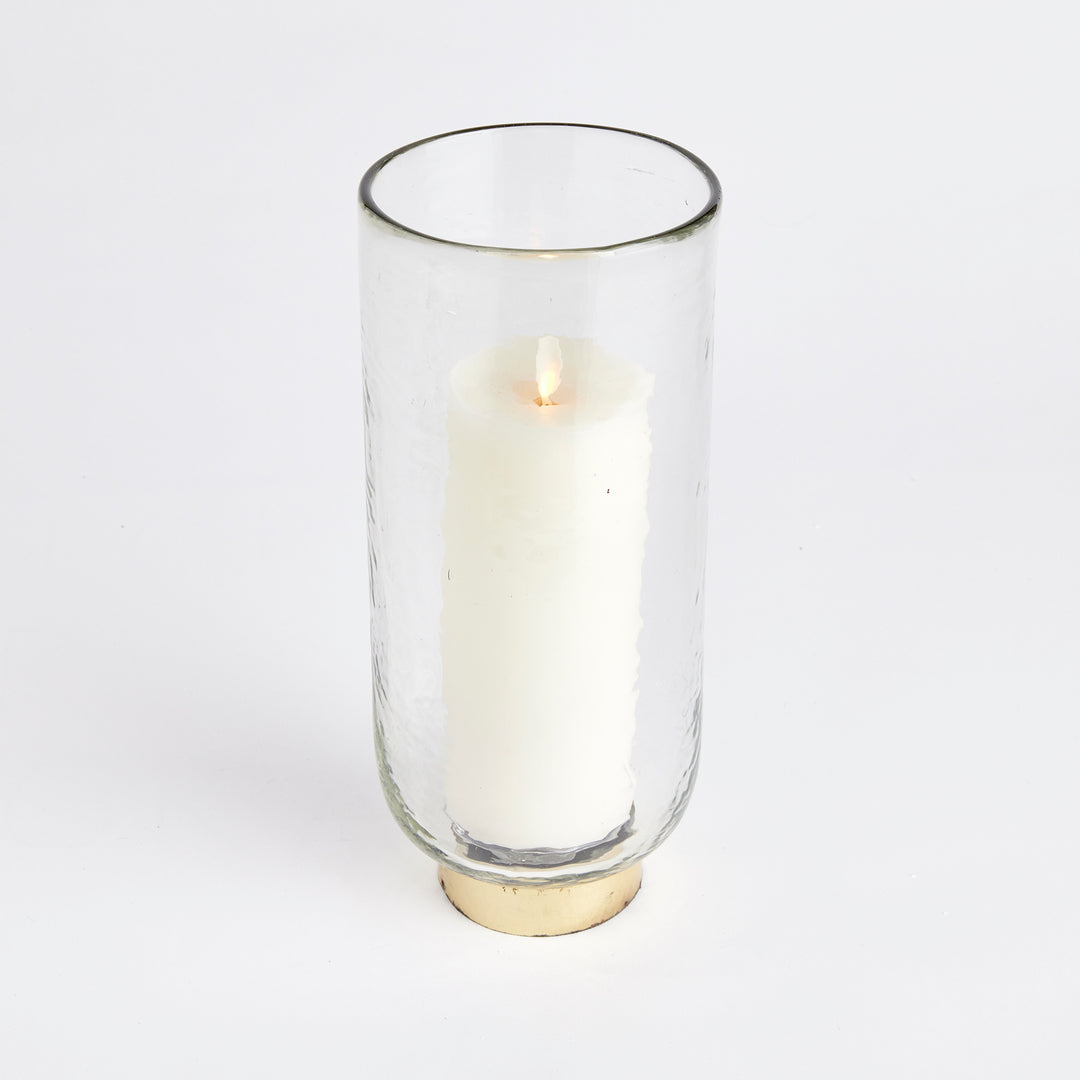 Crafted with precision, this hurricane candle holder showcases a thick, hammered glass and a melted uneven edge, imbuing it with artisanal charm. Complemented by a hammered gold rim base, it serves as a refined accent for any console, bookshelf, or mantel. Boasting superior craftsmanship and a sleek design, this piece is guaranteed to elevate the aesthetic of any space.