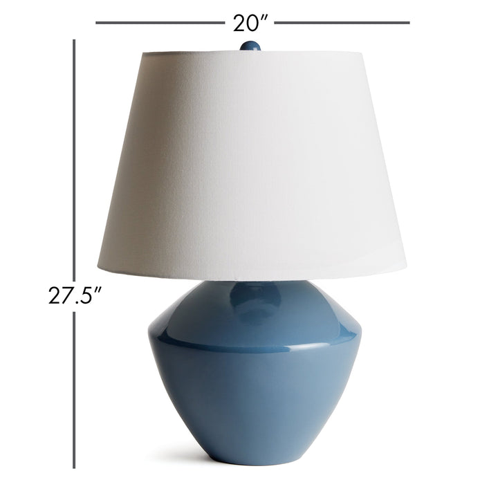 Crafted from a wooden mold dating back centuries, this stunning table lamp boasts a timeless silhouette and a deep blue finish. Topped with a tapered fabric shade, it adds a touch of history and elegance to any room, whether it be a family room, study, or bedroom. This ceramic blue table lamp is a dynamic addition to any space.