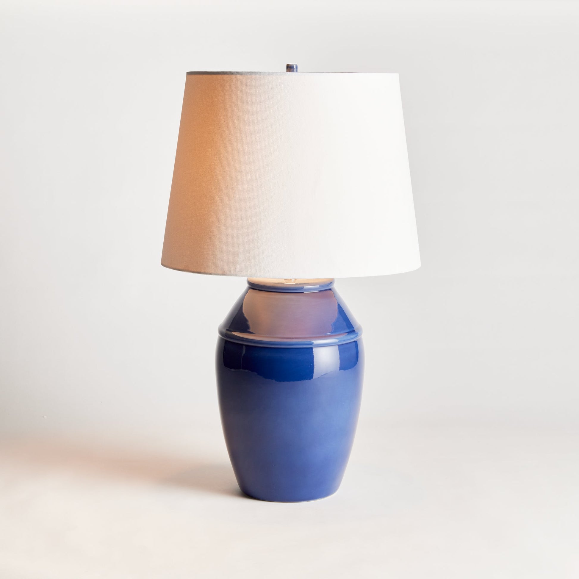 Constructed with a ceramic body and adorned with a deep, luxurious glaze, this coastal-inspired lamp exudes elegance. Enhancing its design, the wide drum shade is crafted from soft white linen, providing a striking contrast. Whether placed on a bedside table, console, or study desk, this lamp is a stunning and practical addition to any space. Its timeless blue and white color combination adds a touch of classic beauty.