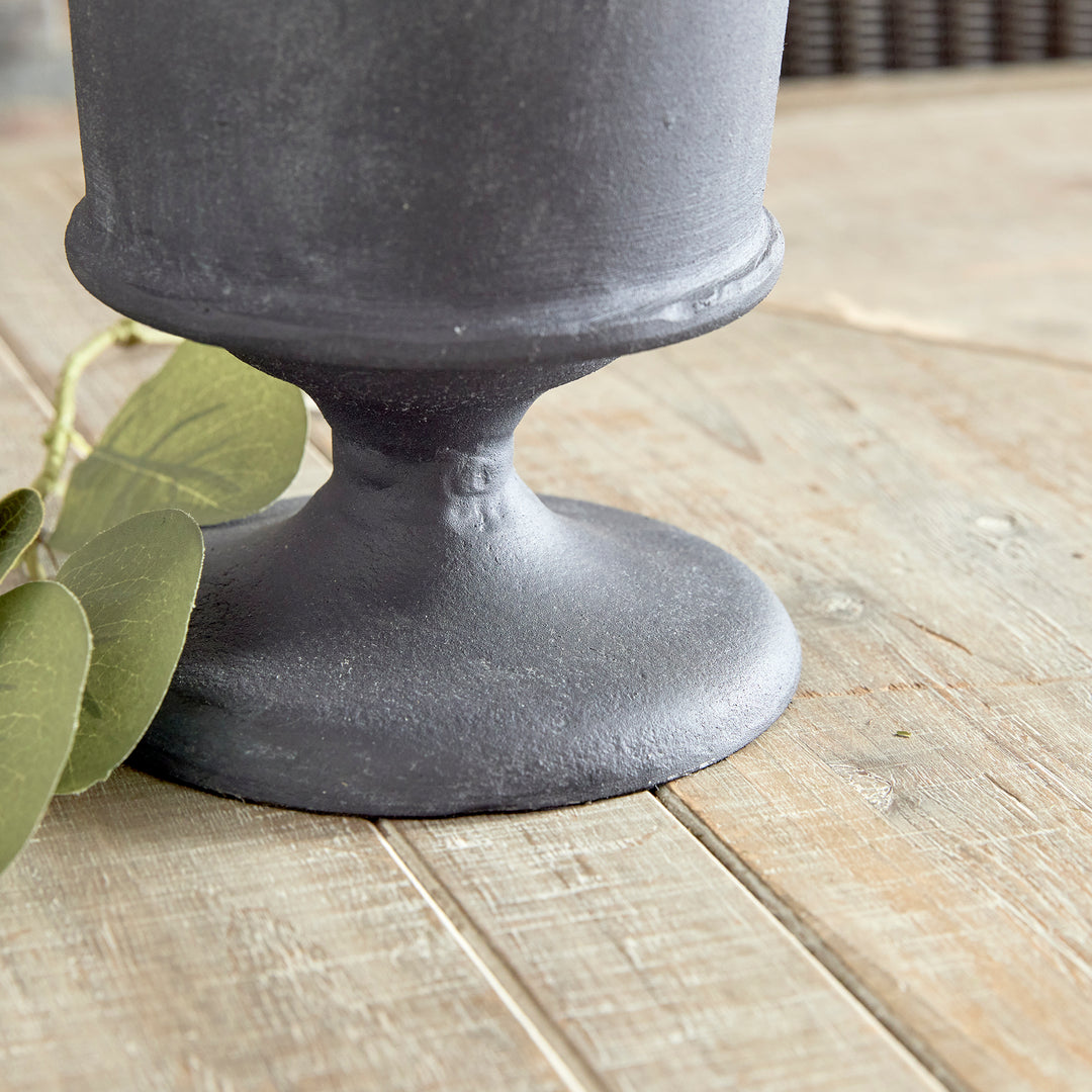 Closeup of decorative metal urn vase pedestal base with aged zinc finish in architectural style