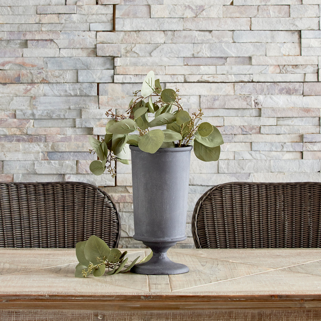 Aged zinc decorative metal urn vase styled with greenery on console table in modern organic style