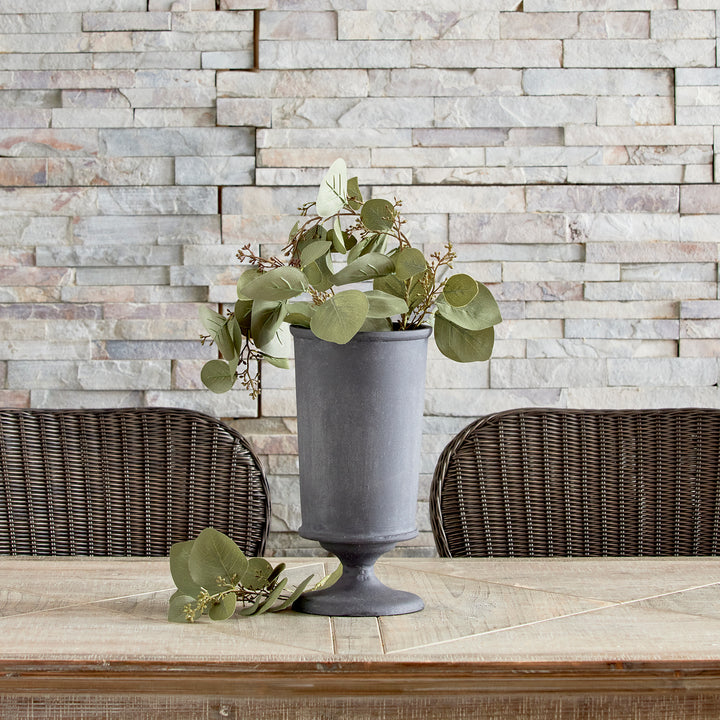 Aged zinc decorative metal urn vase styled with greenery on console table in modern organic style