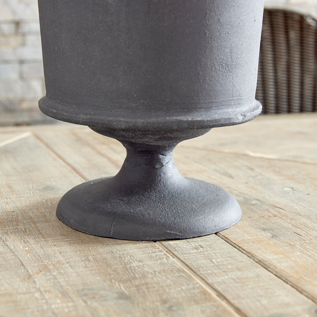 Close view of aged zinc pedestal base on decorative metal urn vase in architectural style