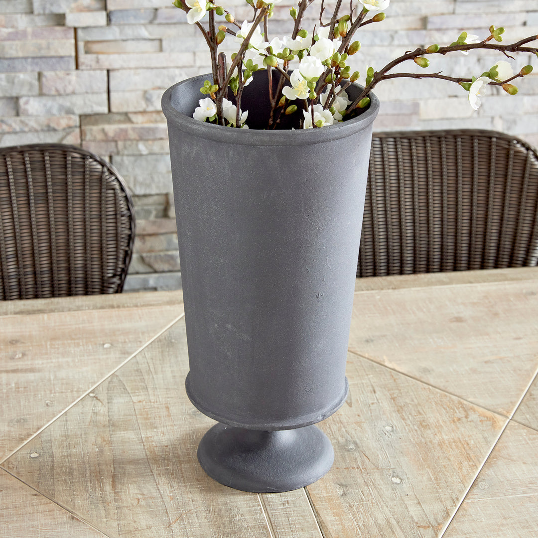 Small decorative metal urn vase with pedestal base styled on tabletop in transitional interior style