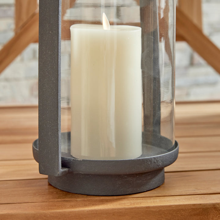 Close-up detail of outdoor hurricane candle holder with glass cylinder and layered pillar candles – Modern Organic style.