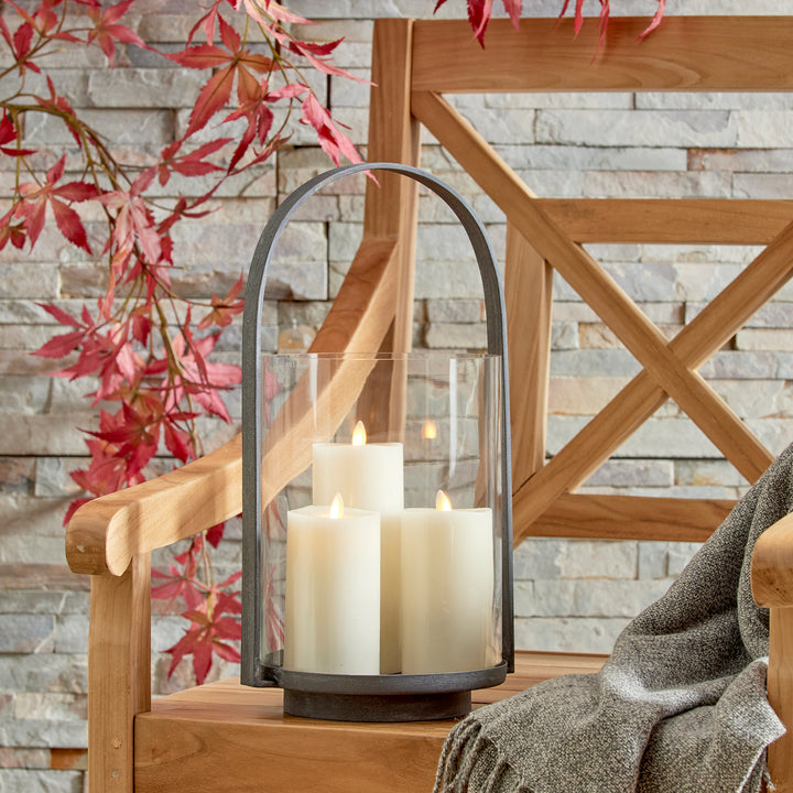 Outdoor hurricane candle holder styled on a wood deck with layered natural textures and aged zinc finish – Modern Organic style.
