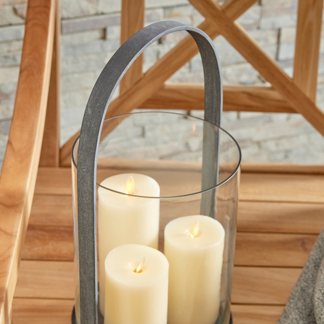 Close-up detail of outdoor hurricane candle holder with curved metal frame and aged zinc finish – Industrial Outdoor style.