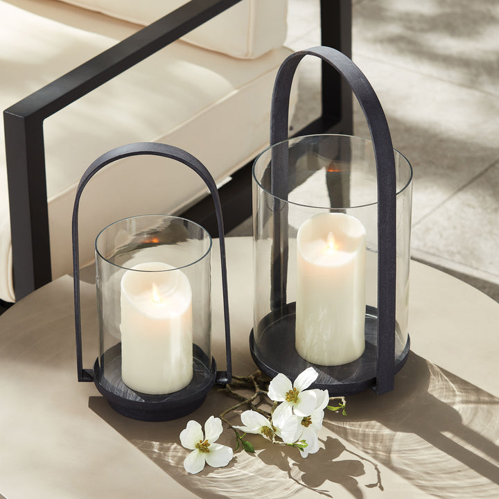 Outdoor hurricane candle holders styled together beside seating with warm candlelight and aged zinc metal frames – European Garden style.