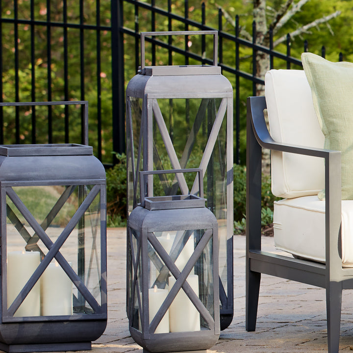Grouped outdoor metal lanterns with aged zinc finish styled beside patio seating and layered candle decor – Transitional style.