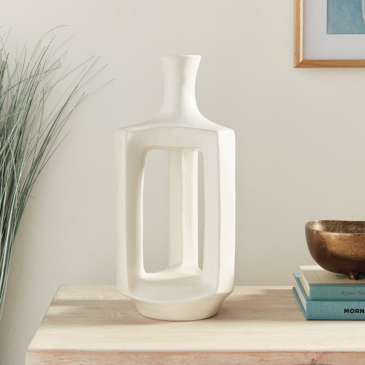 Tall white clay vase beside stacked books and neutral decor, with a narrow neck and open sculptural frame. Modern Organic