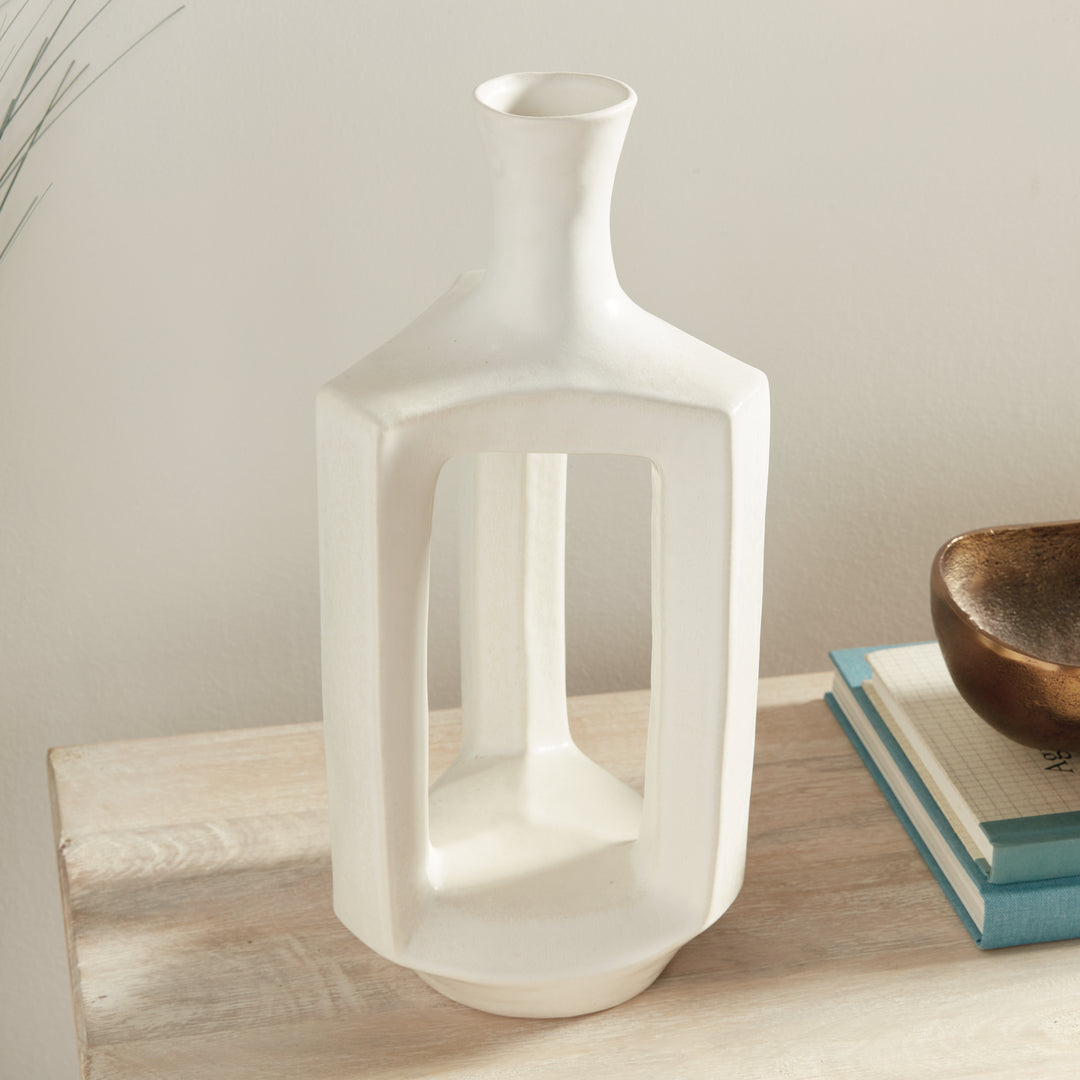 Tall matte white clay vase beside books, showing the open frame, curved neck and gently sloping shoulders. Modern Organic