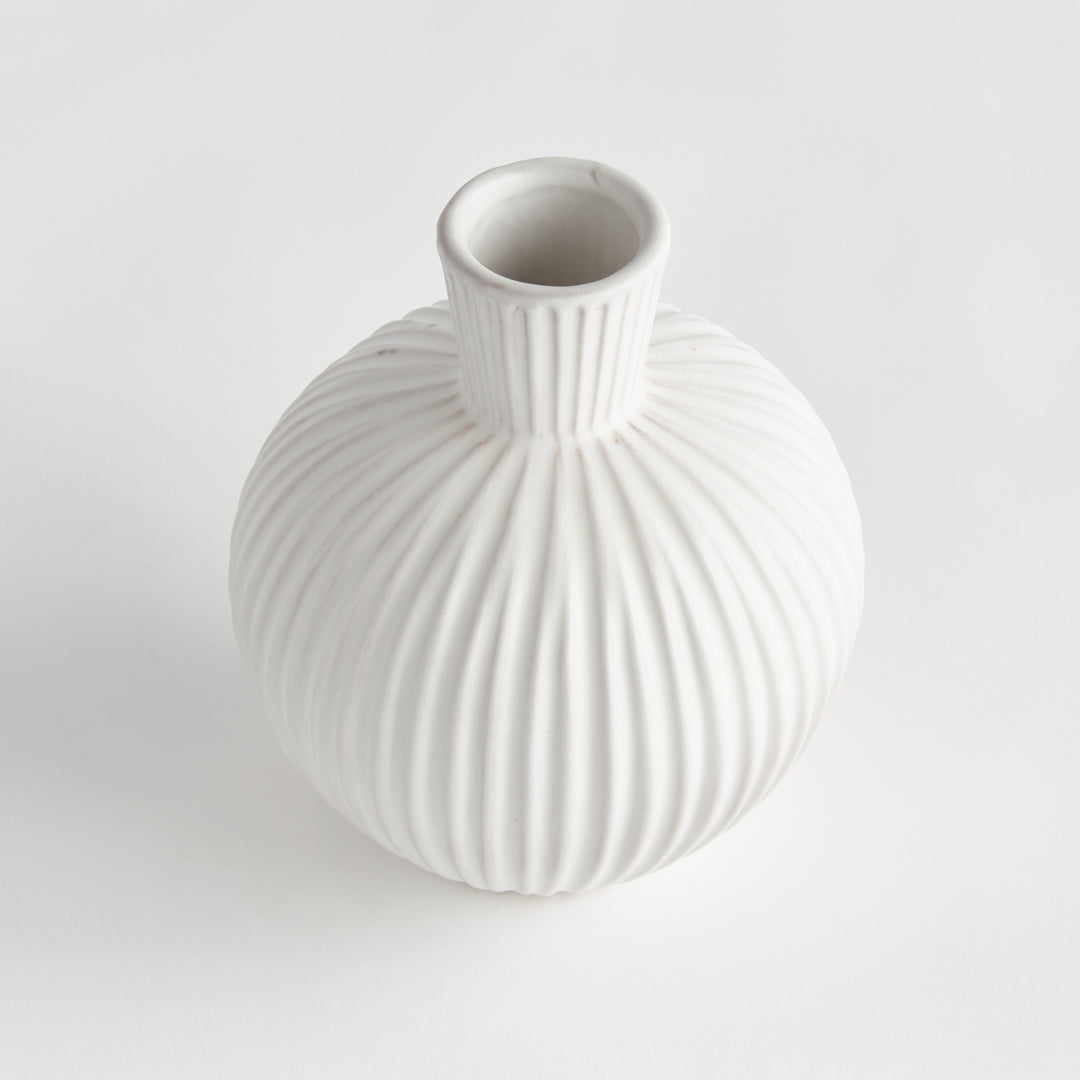 Angled view of a white terracotta vase with an open neck, rounded shoulders and deeply ribbed circular body. Transitional