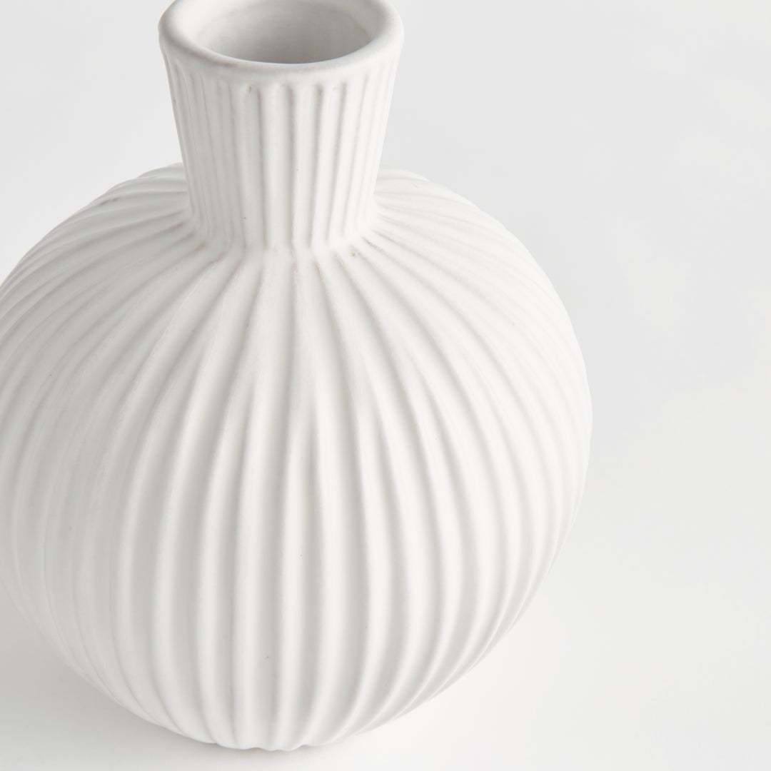 Close view of a white ribbed terracotta vase showing its round body, raised vertical lines and narrow neck. Transitional
