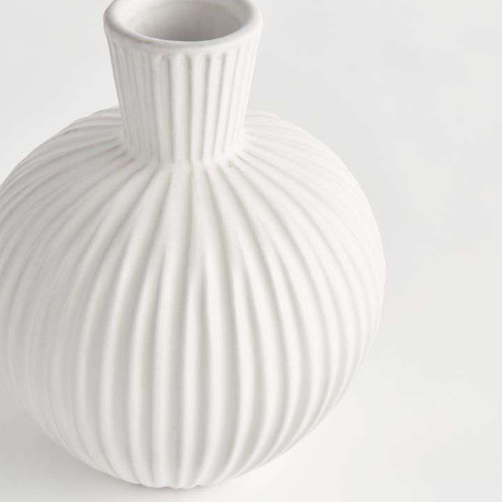 Close view of a white ribbed terracotta vase showing its round body, raised vertical lines and narrow neck. Transitional