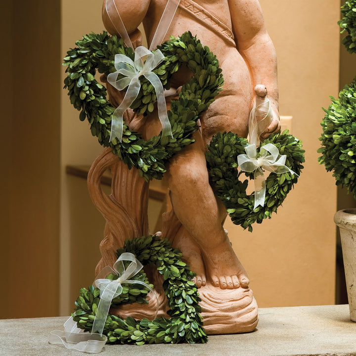 Three Amity preserved boxwood hearts with pale ribbon bows displayed beside a carved figure on a pale ledge. Transitional