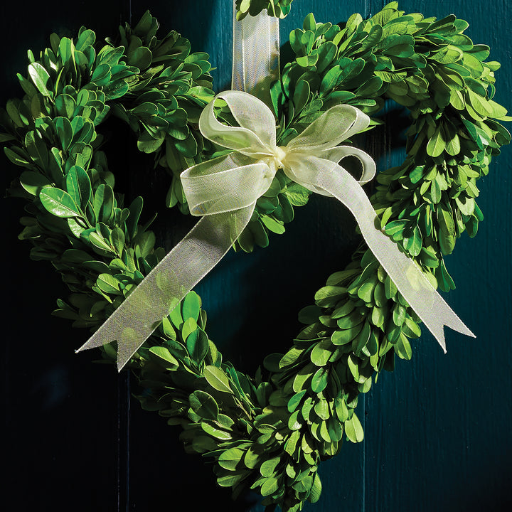 Fine detail of an Amity heart wreath showing dense preserved green boxwood leaves and a pale sheer ribbon bow. Transitional