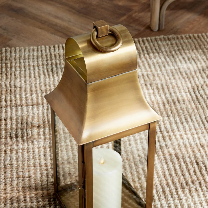 Low angle of small antique brass lantern on textured rug, styled with LED candle for indoor décor – Transitional Classic Lantern