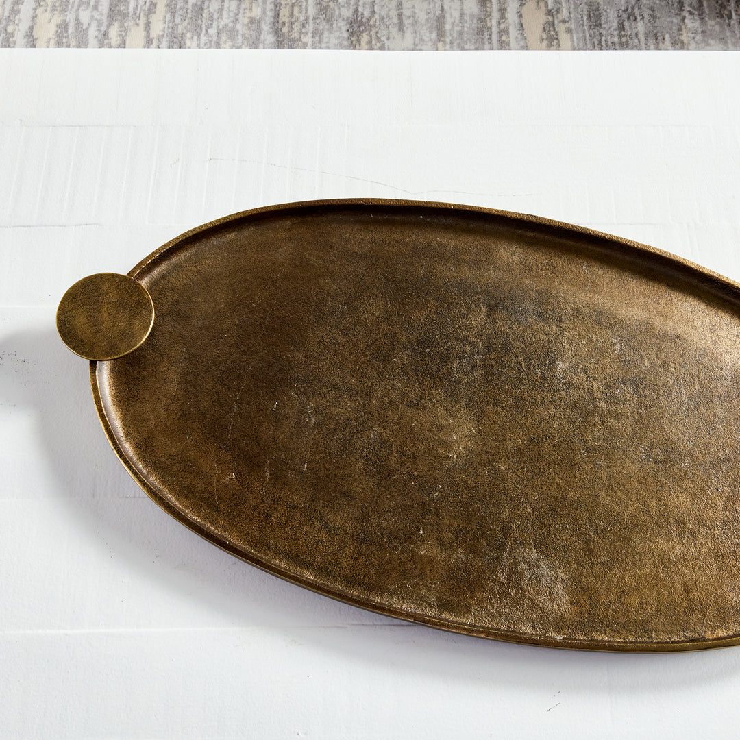 Antique brass oval aluminum decorative tray showing textured interior, raised rim and round handle from above – Transitional.