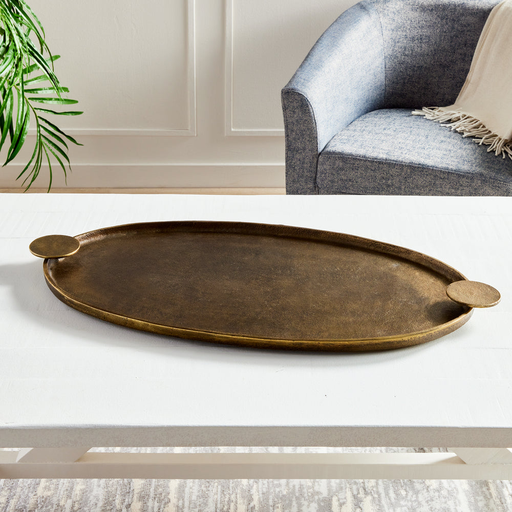 Antique brass oval decorative tray with round handles displayed empty on a white living room coffee table – Transitional.