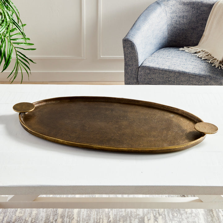 Antique brass oval decorative tray with round handles displayed empty on a white living room coffee table – Transitional.