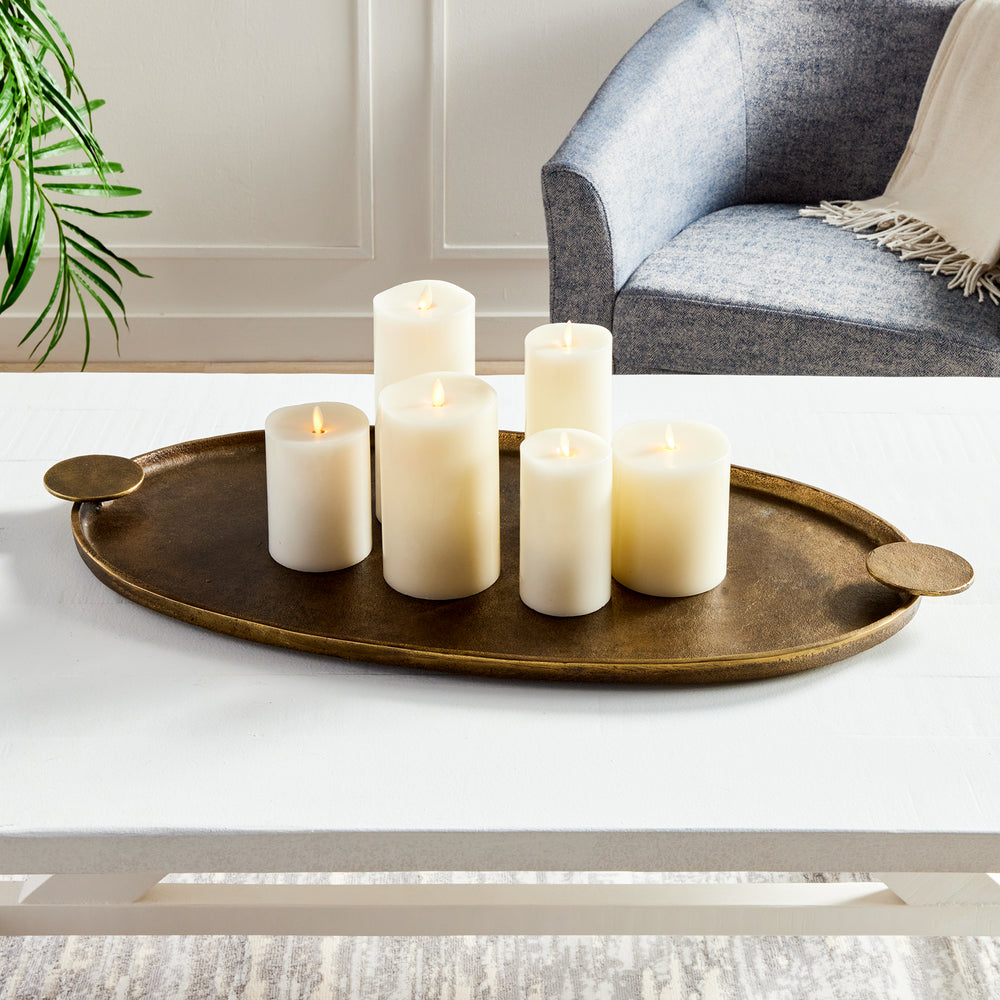 Antique brass oval aluminum tray with ivory pillar candles on a white coffee table in a styled living room – Transitional.