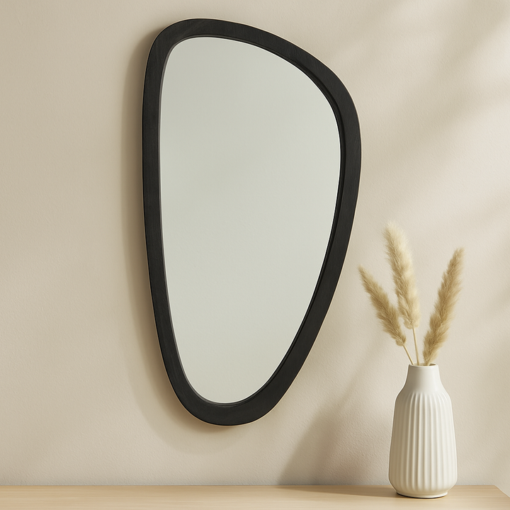Asymmetrical black wall mirror with mid-century modern silhouette styled on a warm neutral wall with natural lighting and clean accents.