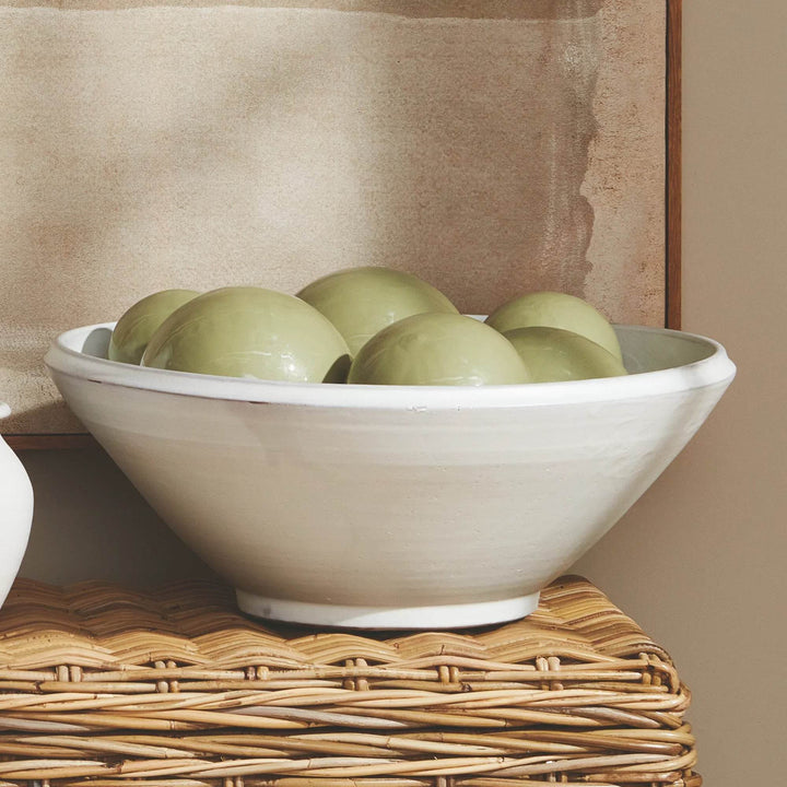 Aveline warm white decorative terracotta bowl filled with green orbs on a woven surface beside framed art. Modern Organic