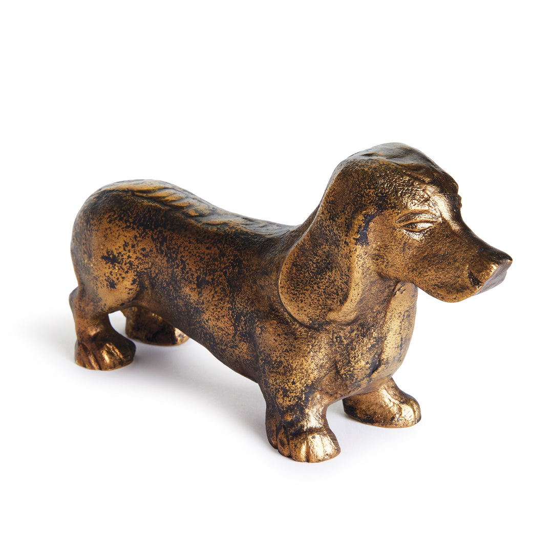 Baxter cast aluminum dachshund sculpture with antique brass finish, short legs and long ears on a pale background. Eclectic