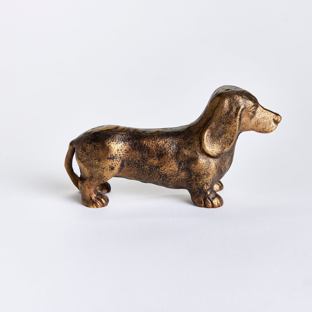 Side view of Baxter dachshund sculpture showing its elongated body, short legs and antique brass finish on white. Eclectic