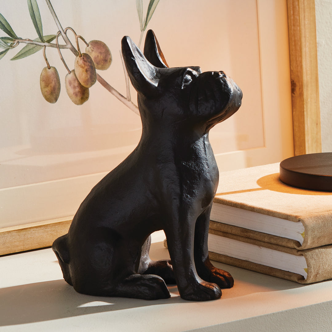 Aluminum dog sculpture placed in shadowed shelf vignette, matte noir finish catching ambient light across its curved silhouette.