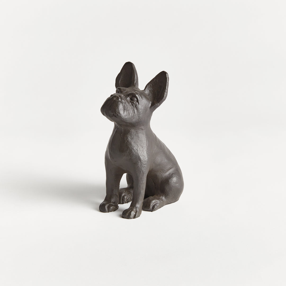 Small aluminum dog sculpture photographed against white background, seated upright with compact, expressive silhouette.