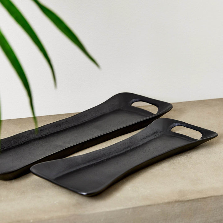 Pair of black trays placed in soft natural light beside a woven chair – Urban Contemporary.

