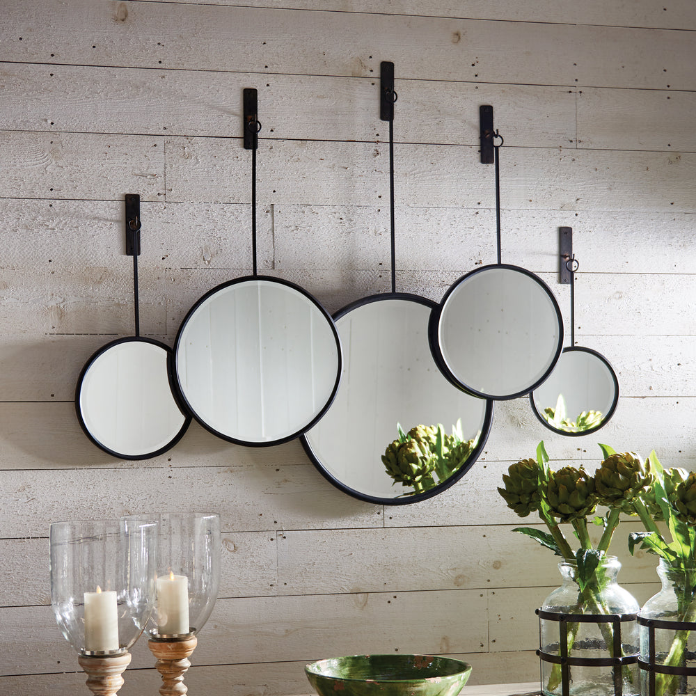 A set of five round black-framed mirrors hang from rods on a white shiplap wall in an industrial coastal interior.