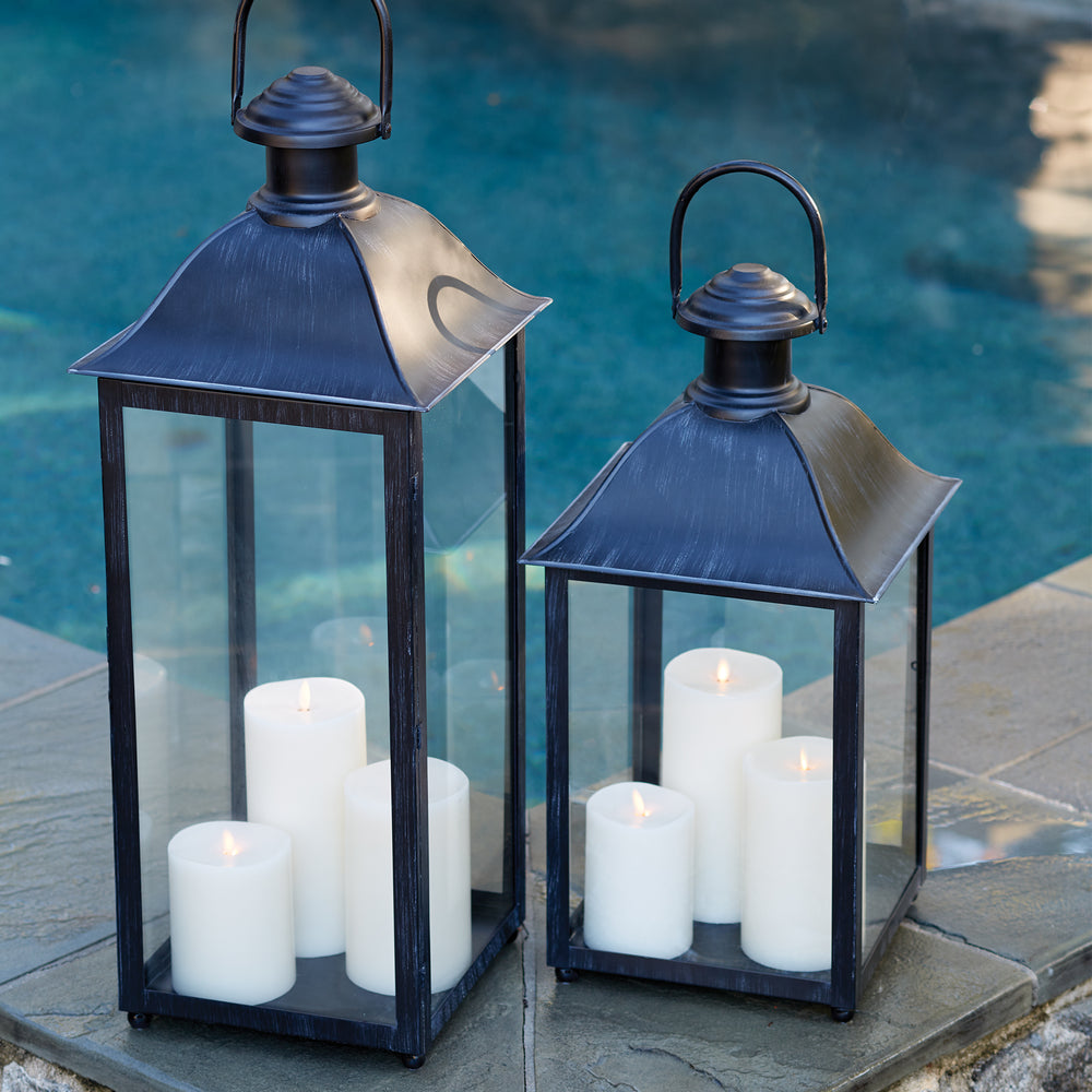 Set of black candle lanterns by the pool with candles glowing inside at dusk
