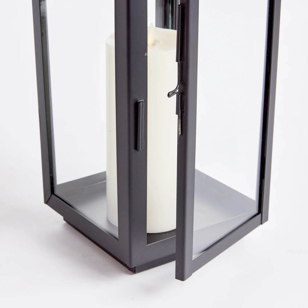 Detail of lower frame, hinged door and latch on black outdoor lantern with glass panels; candle inside on base – Transitional Decorations
