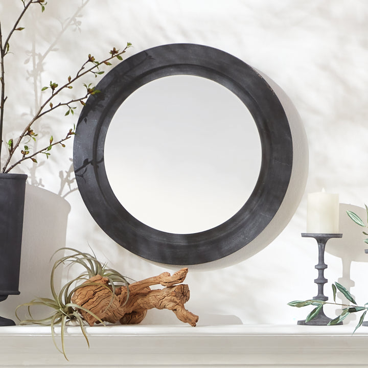 Detail of black round wall mirror mounted on white mantle with taper candles, driftwood, and ceramic vase decor.