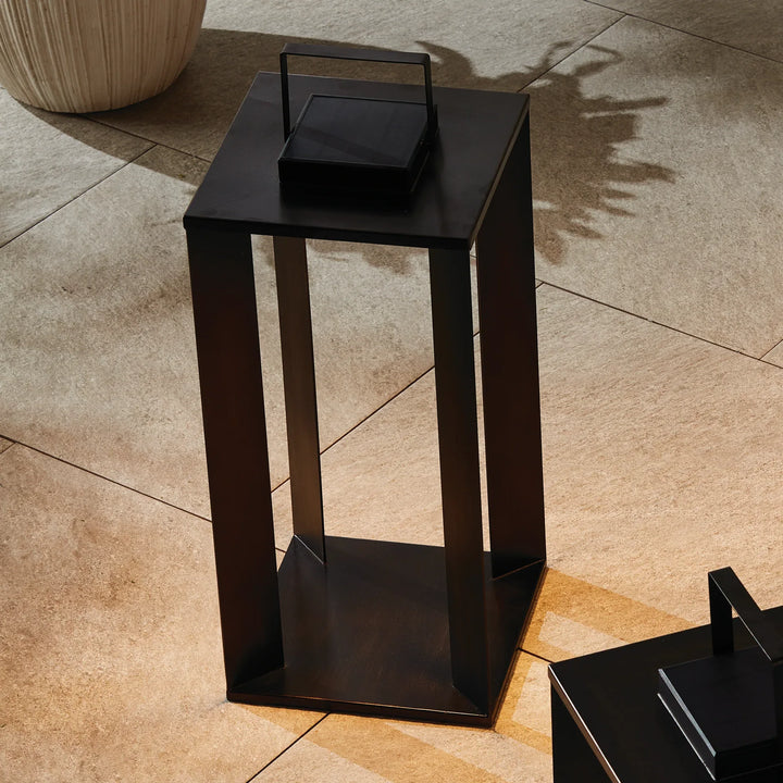 Matte black solar LED lantern styled on outdoor floor with warm glow showcasing modern pathway lighting