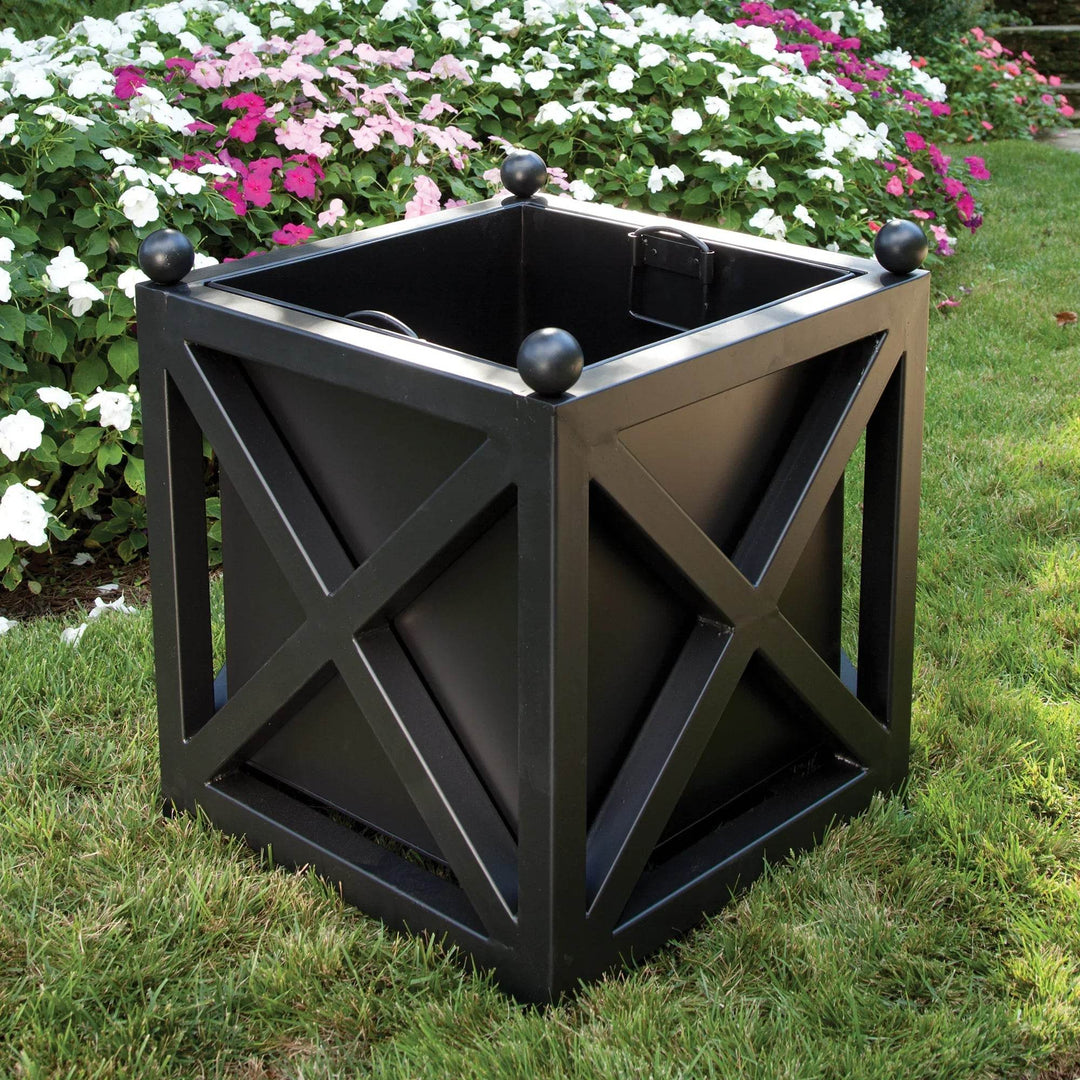 Large black metal planter with ball finials in blooming garden with colorful flowers