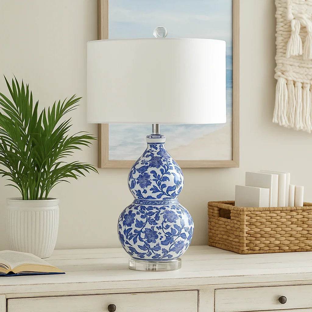 A photograph features an elegant blue and white Chinoiserie table lamp styled in a coastal room with natural light, woven textures, and seaside decor.