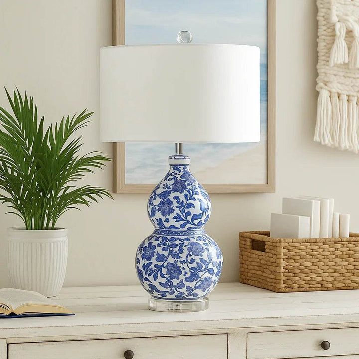 A photograph features an elegant blue and white Chinoiserie table lamp styled in a coastal room with natural light, woven textures, and seaside decor.
